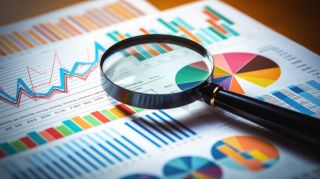 Printed business documents with colorful charts and graphs being analyzed through a magnifying glass