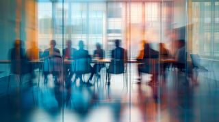 Group of professionals engaged in brainstorming session inside glass-partitioned boardroom - business meeting concept with blurred effect